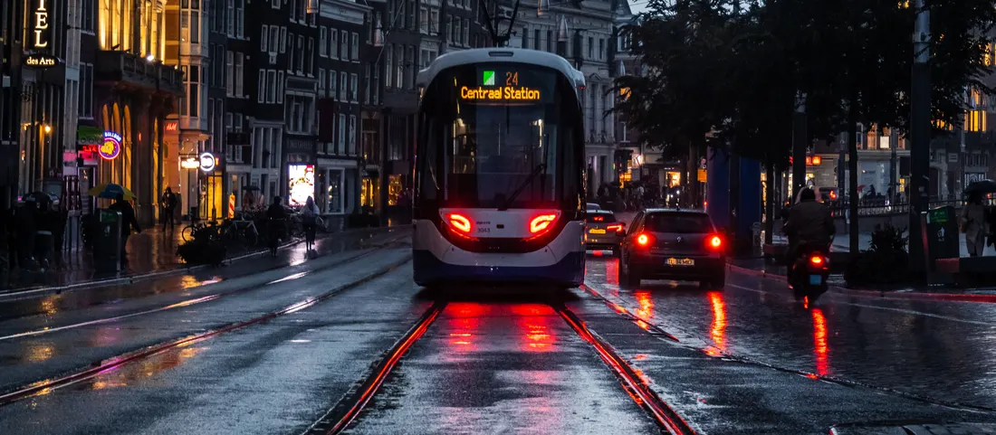 A tram on wet tram tracks under a grey Amsterdam sky