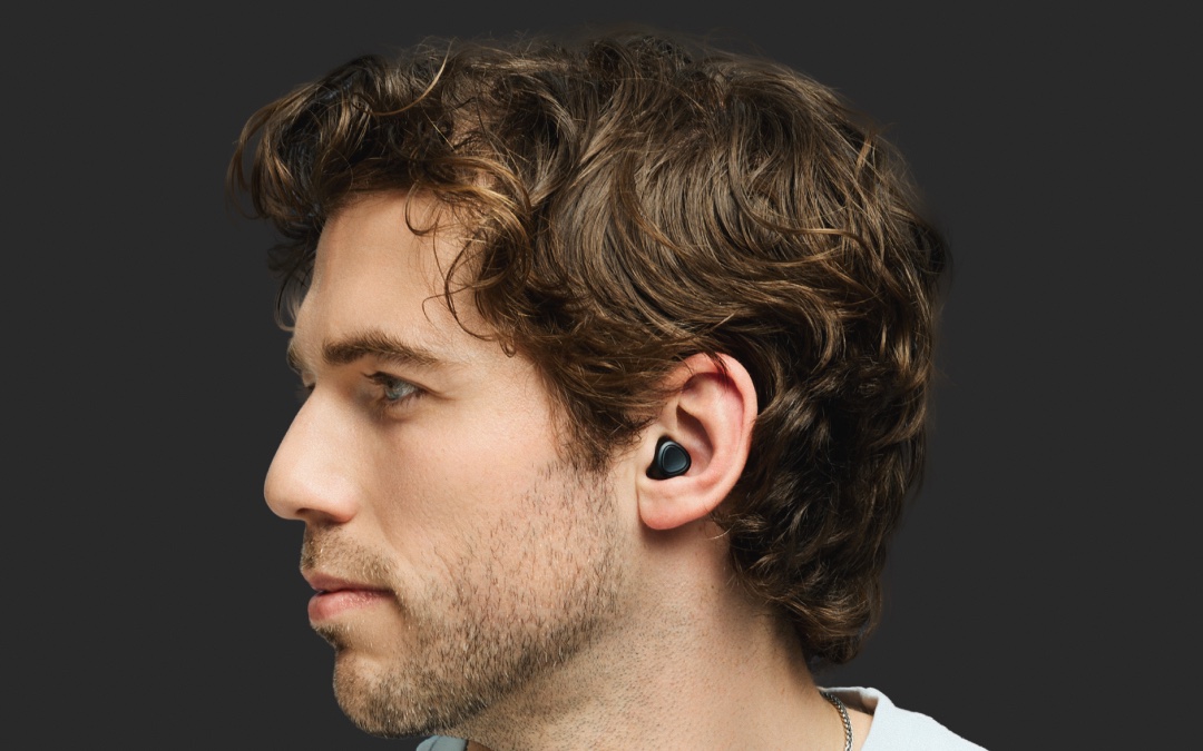 A person in profile wearing a black Unplugs earplug, which sits nearly flush inside the ear